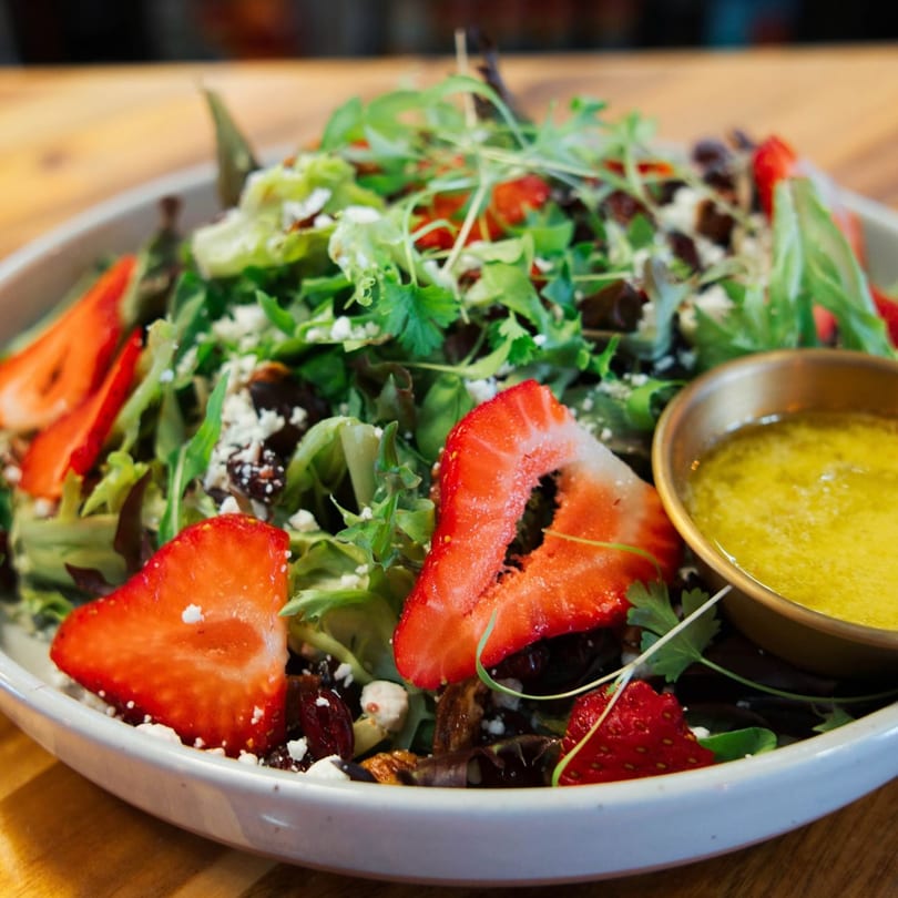 Meating Ground Cafe's fresh salad with strawberries, feta, mixed greens, and a side of dressing.