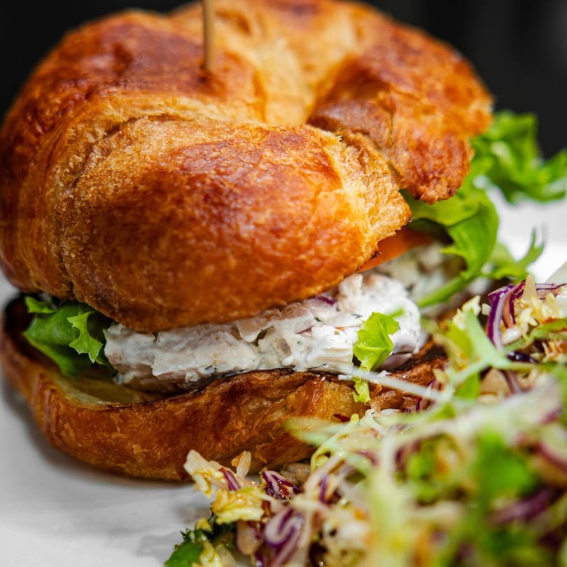 Chicken salad croissant sandwich with lettuce and a side salad on a white plate.
