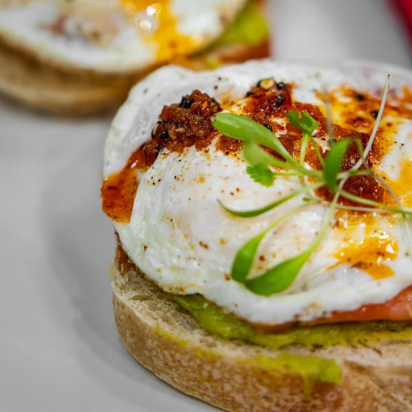 Close-up of a fried egg on toast with avocado, chili oil, and microgreens.