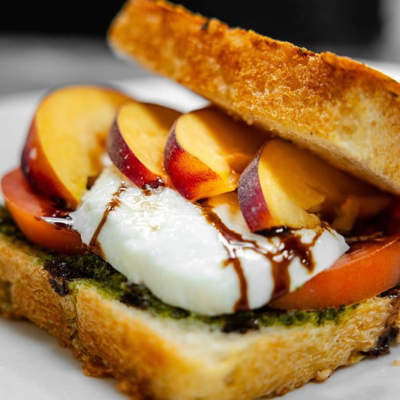 Toasted bread with pesto, sliced tomatoes, fresh mozzarella, peaches, and balsamic glaze.