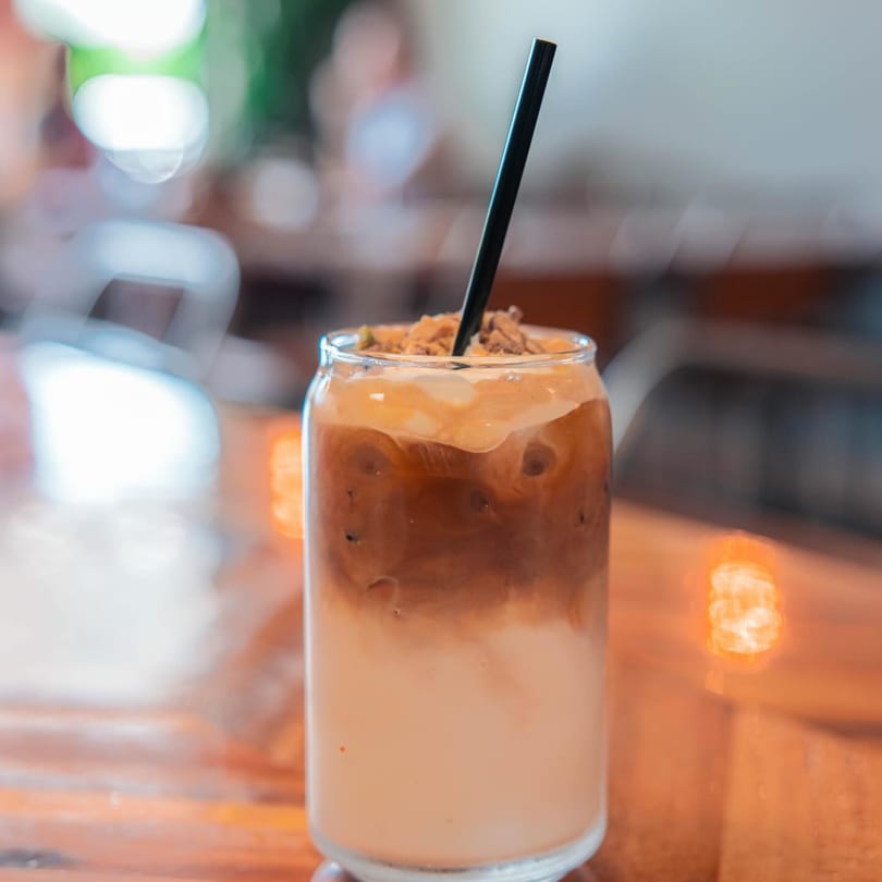 Iced coffee with milk, whipped cream, and cookie crumbles, served in a glass with a black straw.