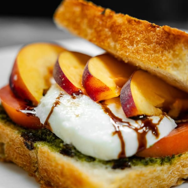 Toasted bread with pesto, tomato, mozzarella, sliced peaches, and balsamic glaze.